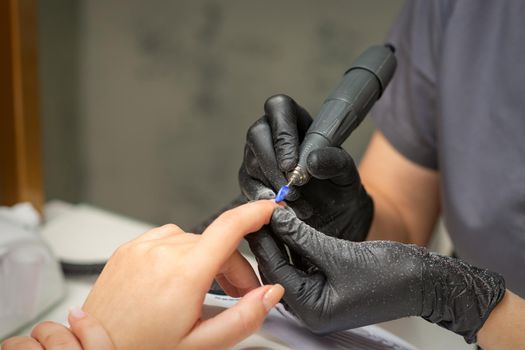 Manicurist removes nail polish uses the electric machine of the nail file during manicure in a nail salon