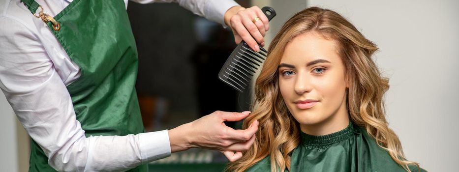 Hairdresser making hairstyling for the woman while combing with hairbrush, comb in a hair salon