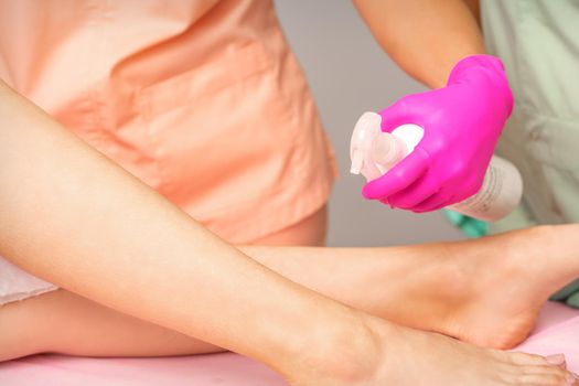 A beautician sprays a disinfectant on the feet of a young woman before the epilation procedure. Foot depilation