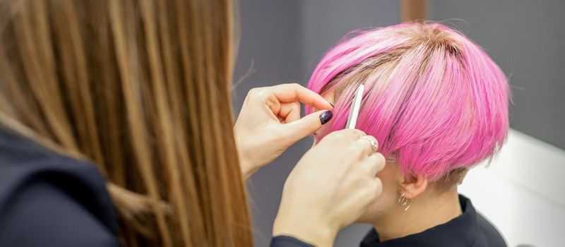 Hairdresser prepares dyed short pink hair of a young woman to procedures in a beauty salon