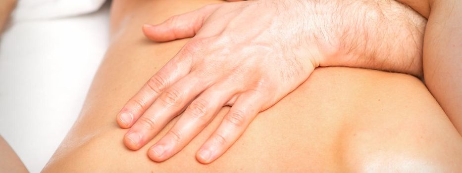 A male physiotherapist stretches the arms on the back of a man lying down, close up