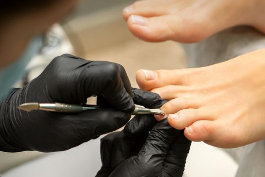 Cuticle Removal on Toes. Hands in black gloves of pedicure master remove cuticle on female toes by pusher