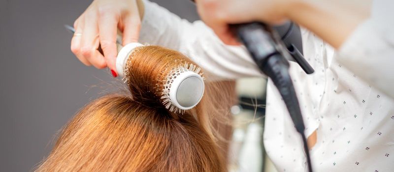 Drying red hair with a hairdryer and round brush, close up