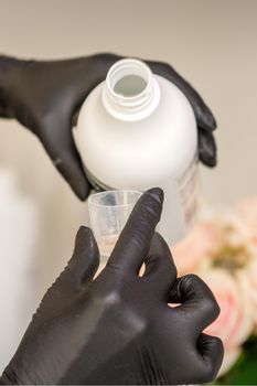 A hairdresser in black gloves is preparing hair dye with a bottle in a hair salon, close up