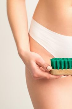 A woman in white panties holds a clothes brush on a white background. Depilation on the bikini zone