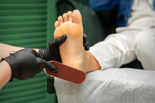 Peeling of Heels. Hands of pedicure master scrape dead from heel skin by special grater in spa salon