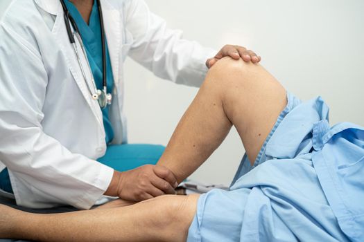 Asian doctor physiotherapist examining, massaging and treatment knee and leg of senior patient in orthopedist medical clinic nurse hospital.