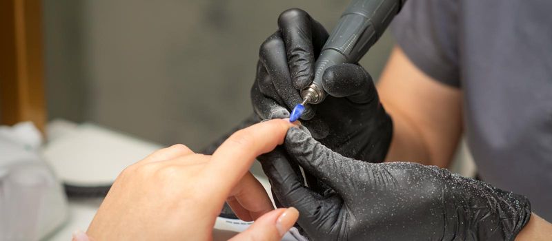 Manicurist removes nail polish uses the electric machine of the nail file during manicure in a nail salon