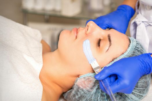 Face peeling at the beautician. Facial treatment. The beautician applies a cleansing face mask to the female patient