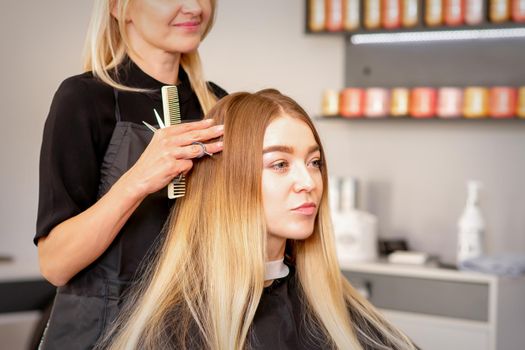 Gorgeous blonde long hair woman and her hairdresser looking and checking out hairstyle. Beautiful hairstyle of a young blonde woman after dying hair in a beauty salon, results of hair treatment