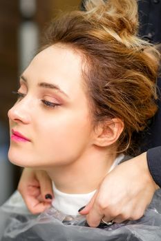 A hairdresser is covering a female neck with a cape for a female client in a beauty salon, close up