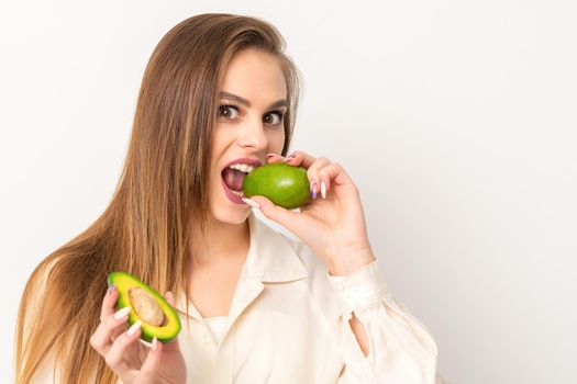 Diet nutrition. Beautiful young caucasian woman biting organic green avocado on white background. Healthy lifestyle, health concept