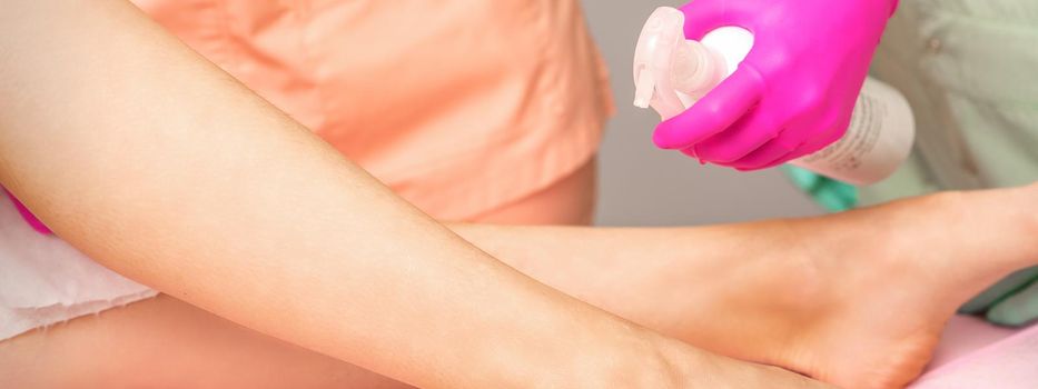 A beautician sprays a disinfectant on the feet of a young woman before the epilation procedure. Foot depilation