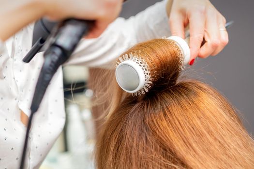 Drying red hair with a hairdryer and round brush, close up