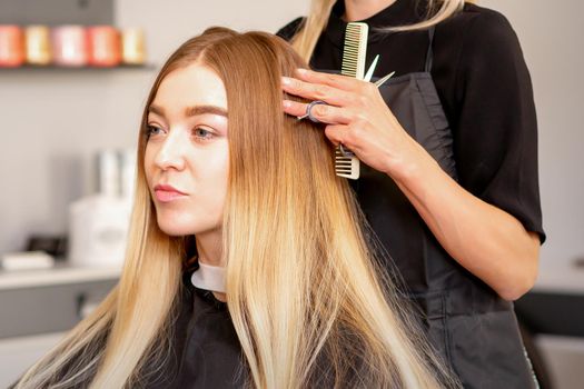 Gorgeous blonde long hair woman and her hairdresser looking and checking out hairstyle. Beautiful hairstyle of a young blonde woman after dying hair in a beauty salon, results of hair treatment