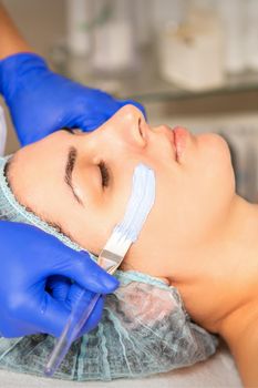 Face peeling at the beautician. Facial treatment. The beautician applies a cleansing face mask to the female patient