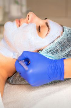 Face peeling at the beautician. Facial treatment. The beautician applies a cleansing face mask to the female patient