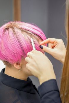 Hairdresser prepares dyed short pink hair of a young woman to procedures in a beauty salon