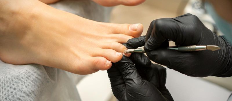 Cuticle Removal on Toes. Hands in black gloves of pedicure master remove cuticle on female toes by pusher