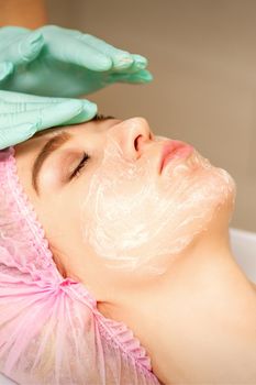 Face peeling at the beautician. Facial treatment. The beautician applies a cleansing face mask to the female patient