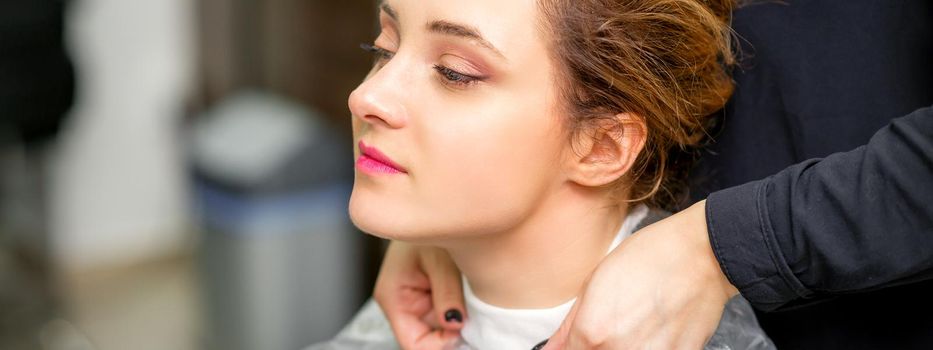 A hairdresser is covering a female neck with a cape for a female client in a beauty salon, close up