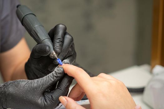 Manicurist removes nail polish uses the electric machine of the nail file during manicure in a nail salon