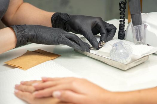 Hands in black gloves of manicurist preparing special nail file equipment for manicure treatment in a beauty salon