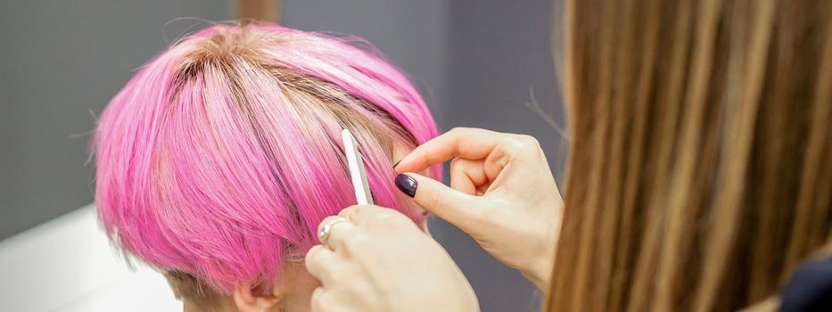 Hairdresser prepares dyed short pink hair of a young woman to procedures in a beauty salon