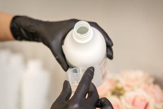 A hairdresser in black gloves is preparing hair dye with a bottle in a hair salon, close up