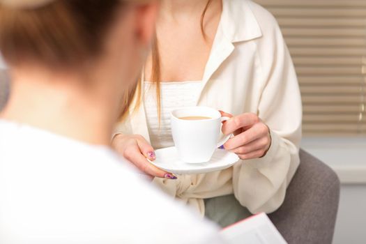 The young caucasian woman has a coffee and appointment with a female doctor in hospital office