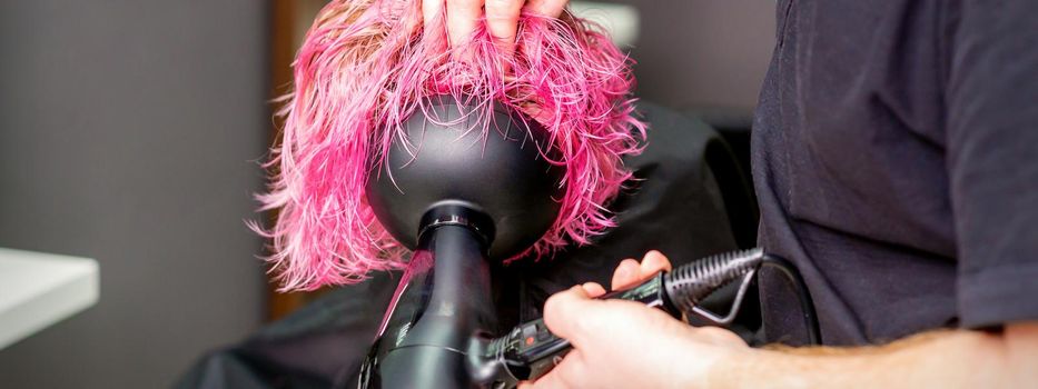 Hair Stylist making hairstyle using hair dryer blowing on wet custom pink hair at a beauty salon