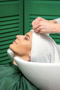 A hairdresser is wrapping a female head in a towel after washing hair in the beauty salon