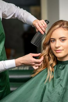 Hairdresser making hairstyling for the woman while combing with hairbrush, comb in a hair salon