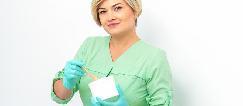 Cosmetician holding a jar of wax for depilation smiling on a white background. Natural product for hair removal. Copy space