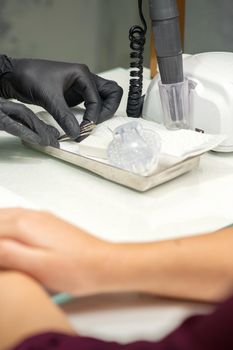 Hands in black gloves of manicurist preparing special nail file equipment for manicure treatment in a beauty salon