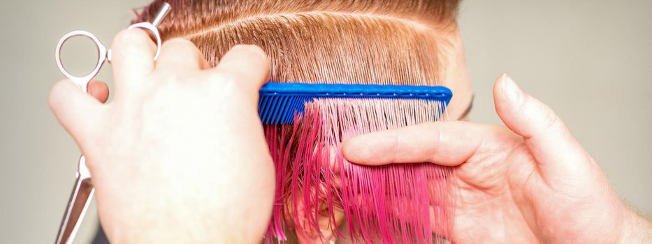 Hands of hairdresser combing hair making short pink hairstyle for a young caucasian woman in a beauty salon