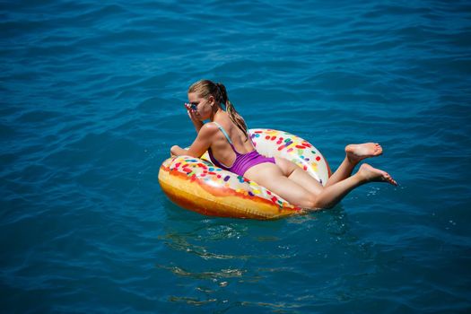 Beautiful young woman in the sea swims on an inflatable ring and has fun on vacation. Girl in a bright swimsuit at the sea under the sunlight