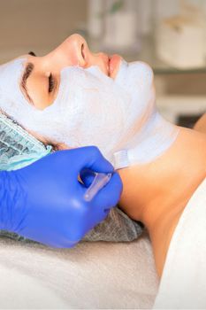 Face peeling at the beautician. Facial treatment. The beautician applies a cleansing face mask to the female patient