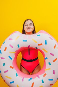 Emotional young woman wearing a pink swimsuit with an inflatable ring isolated on a bright yellow background. Summer hotel pool sea vacation sun tanning concept