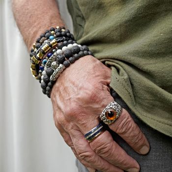 Senior man putting his hand in the pocket of his grey jeans. He wears lava stone and other breaded bracelets and special rings.