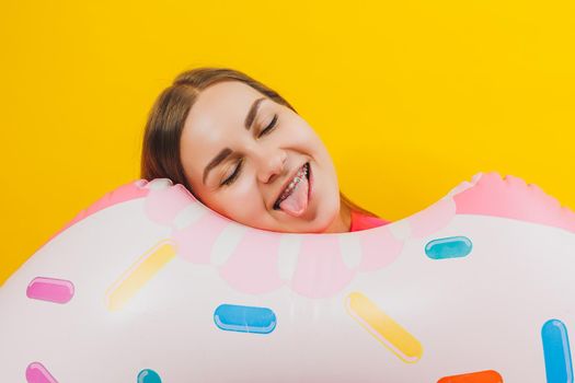 Emotional young woman wearing a pink swimsuit with an inflatable ring isolated on a bright yellow background. Summer hotel pool sea vacation sun tanning concept