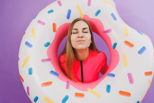 Attractive emotional woman in stylish pink swimsuit with donut inflatable ring on plain background. Beach fashion