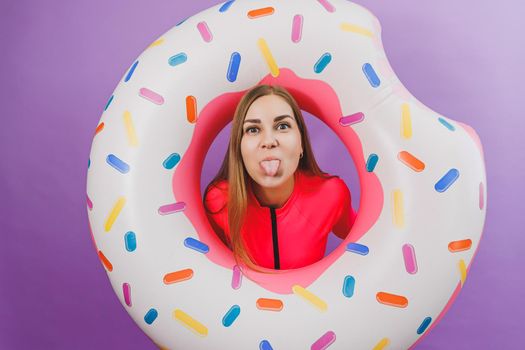 Attractive emotional woman in stylish pink swimsuit with donut inflatable ring on plain background. Beach fashion