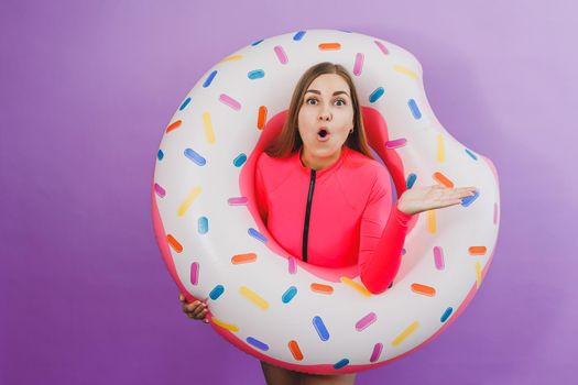 Attractive emotional woman in stylish pink swimsuit with donut inflatable ring on plain background. Beach fashion