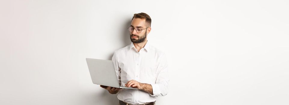 Business. Serious manager working on laptop, standing over white background. Copy space