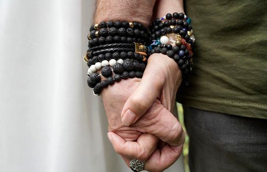 Senior man en woman holding hands. They wear lava stone and other breaded bracelets.