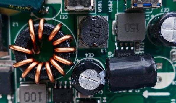 Macro photo of an electronic circuit board of a portable charger. At the right an induction coil with copper wire winding, a toroidal inductor