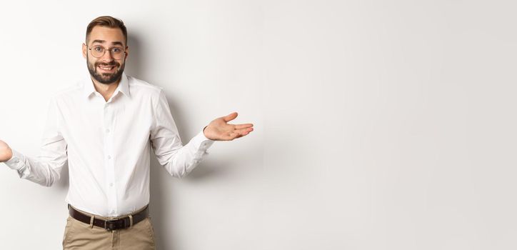 Confused smiling businessman dont know, shrugging and saying sorry, standing over white background.