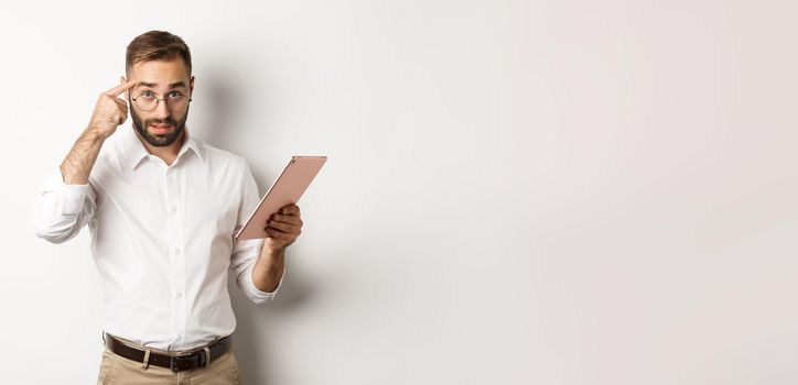 Displeased employer scolding staff while checking report on digital tablet, pointing at head and looking disappointed, standing over white background.