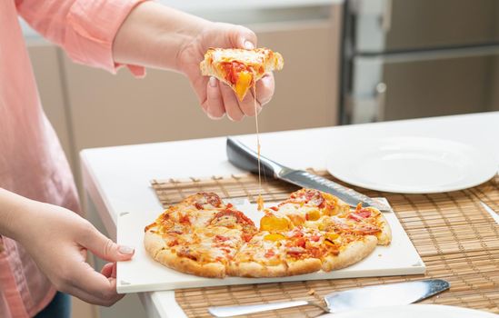 separation of a piece of homemade pizza served on a plate by female hands.